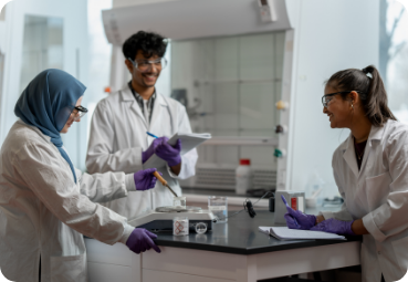 research-page Three researchers in lab coats examine some equipment